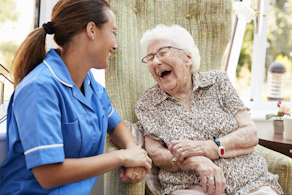 Life Assure Senior Woman Sitting In Chair And Laughing With Caregiver Nurse Blog